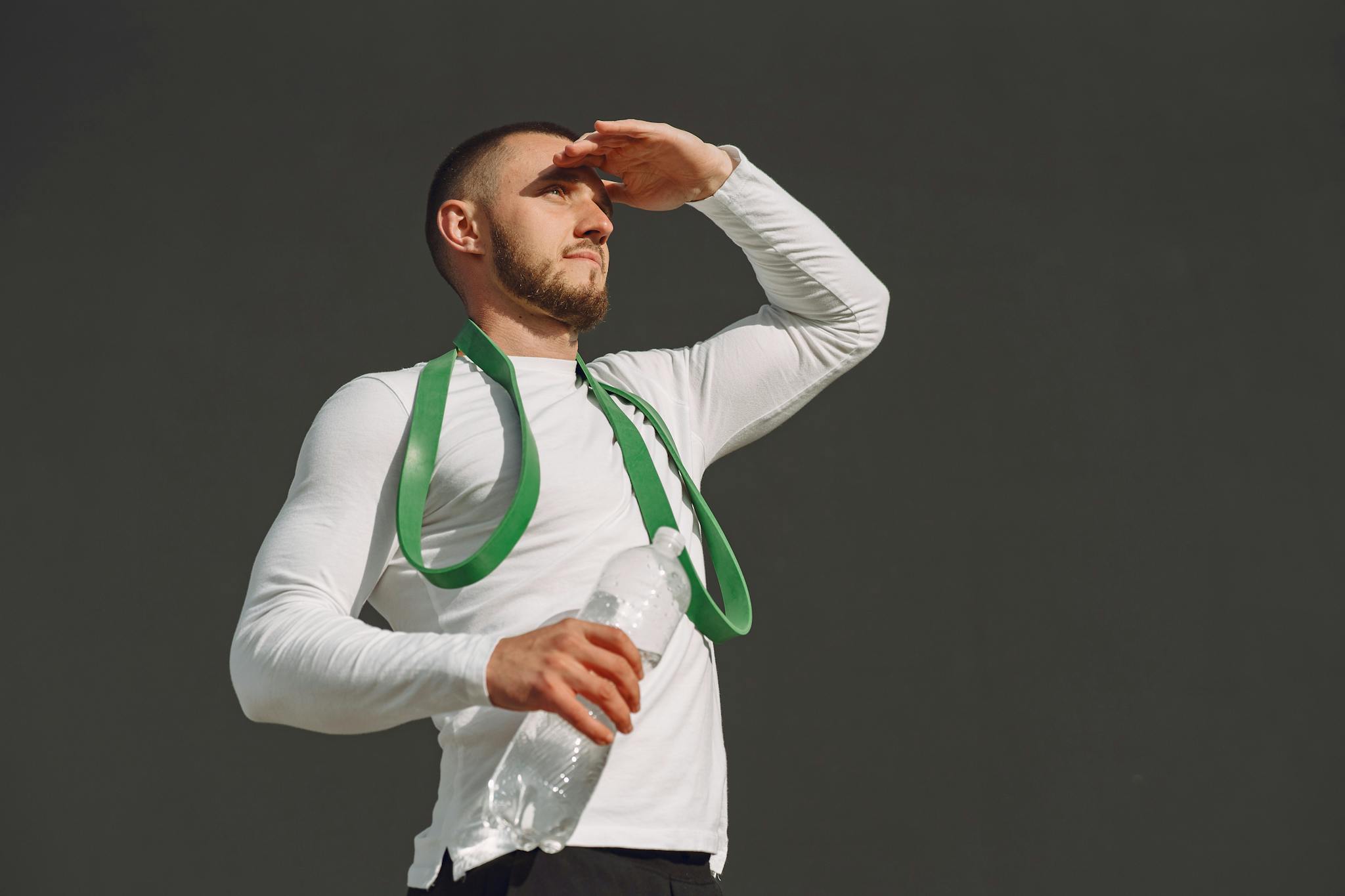 Athletic man in sportswear holding a water bottle and looking ahead outdoors.