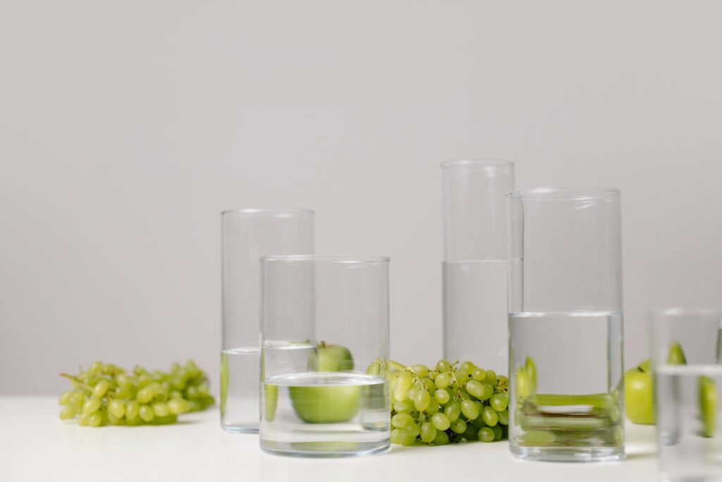 Elegant minimalist setup featuring glasses of water and green grapes on a white table.